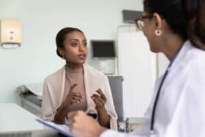 Young African patient woman consulting doctor in clinic, telling healthcare complaints for physician writing notes, talking to medical specialist, asking for treatment, prescription for pills